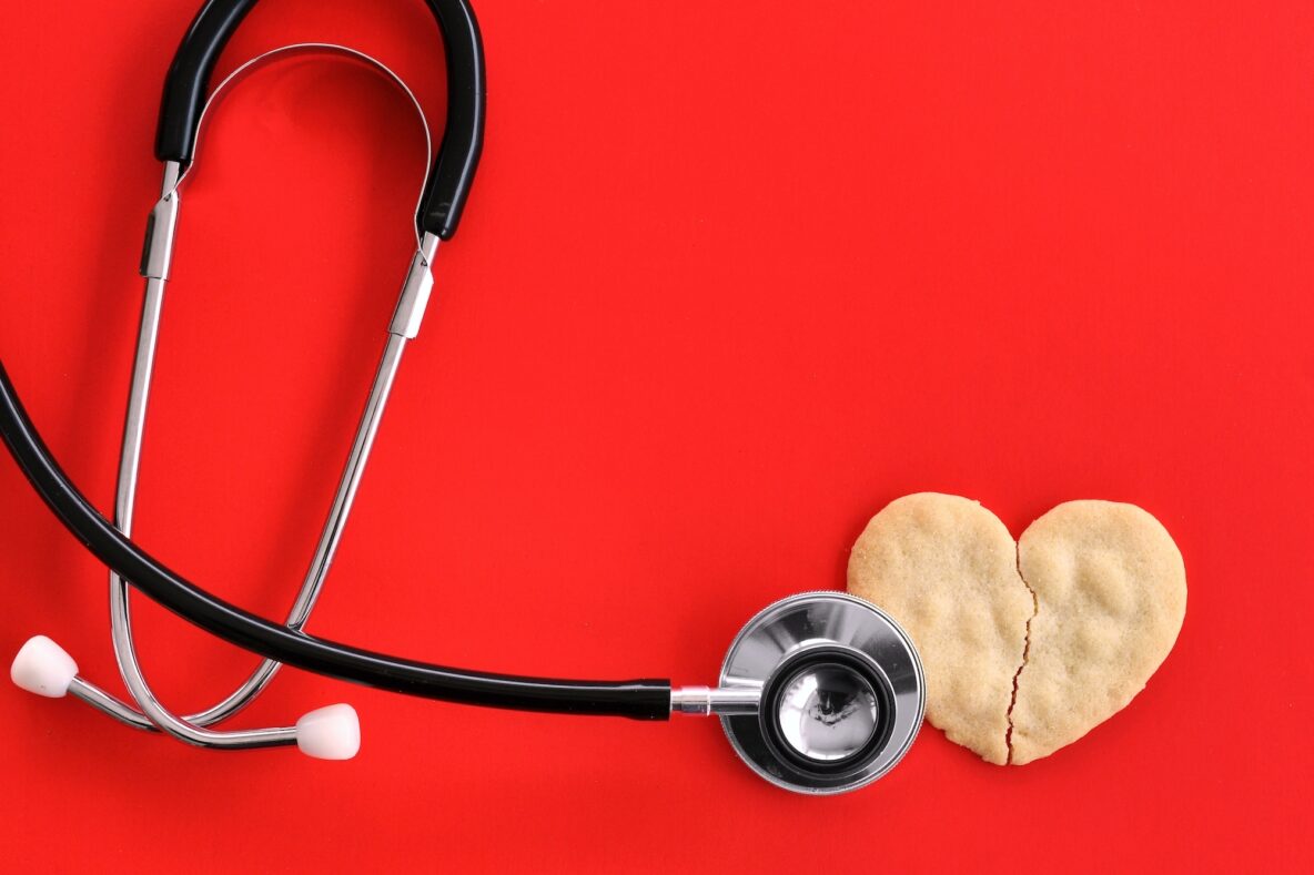 Stethoscope and a cookie shaped like a broken heart on a red background.