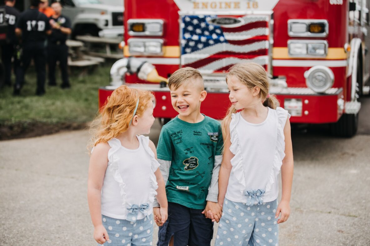 Children holding hands, laughing in front of a fire engine.