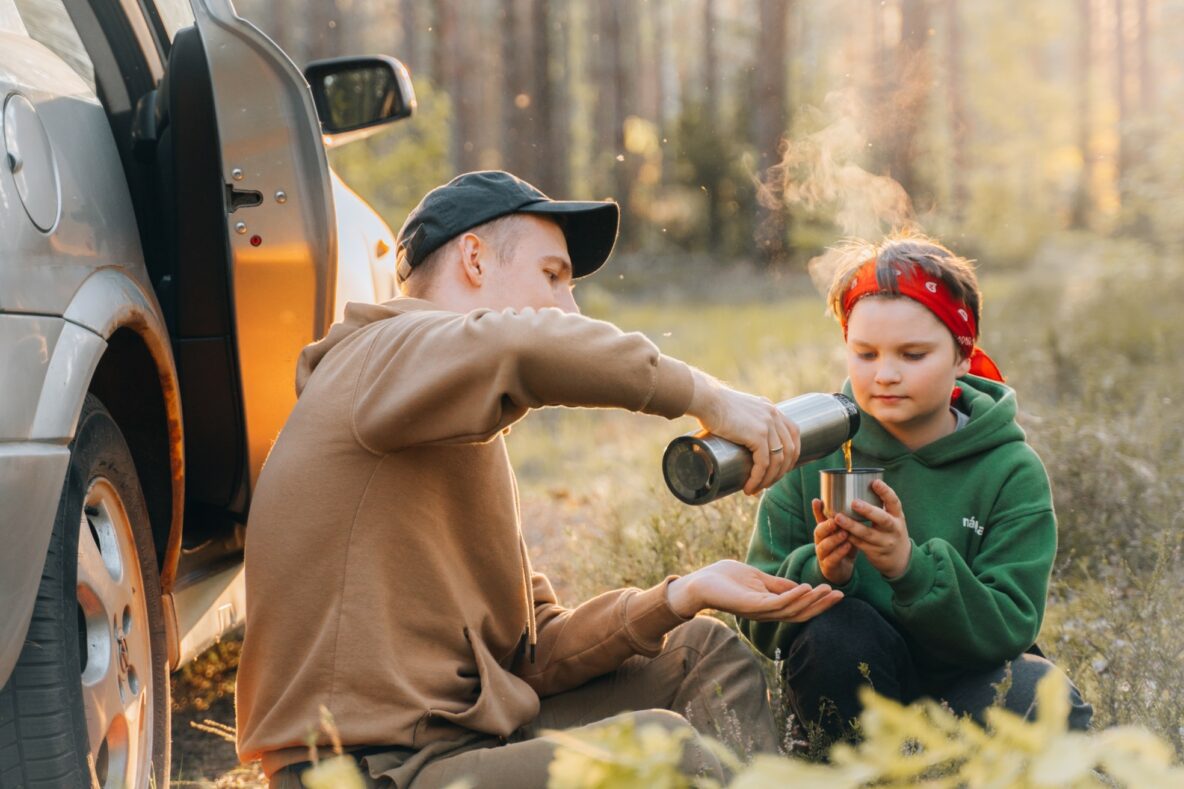 Father and child drinking thermos of hot drink on camping trip